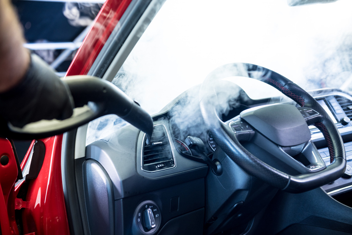 Car service worker cleans interiror with steam cleaner.